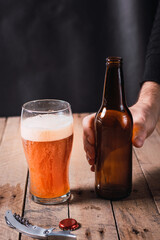 waiter serving craft red beer in a glass bottle on a rustic wooden table and dark environment.