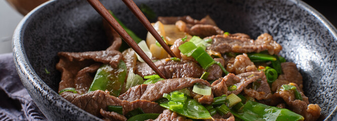 eating chinese beef and snowpeas stirfry in bowl with chopsticks