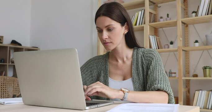 Focused businesswoman doing paperwork working online on laptop sit at home office desk, female entrepreneur professional freelancer using computer software pay bills in app typing at modern workplace