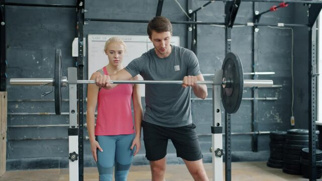 Young girl in sportswear is lifting heavy barbell getting advice from man instructor in gym working out during professional training. People and sports concept.