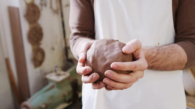 Close up of male potter wearing apron holding lump of clay in ceramics studio - shot in slow motion