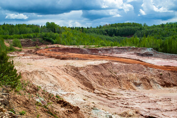 Red clay quarry, green trees and blue sky with beautiful clouds.