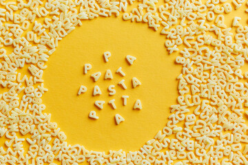 Top view of the macaroni alphabet and the inscription in a circle, on a bright yellow background