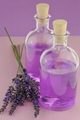 Obraz na płótnie Canvas Lavender water. Lavender Extract.Lavender essence in transparent bottles and sprigs of lavender flowers on a combined pink-purple background.Organic natural cosmetics concept. Lavender cosmetics