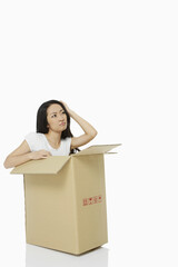 Woman sitting inside of a cardboard box, looking confused