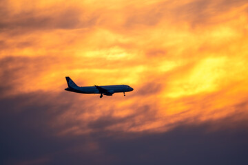 Airplane landing on orange cloudy dramatic sunset. Travel concept.