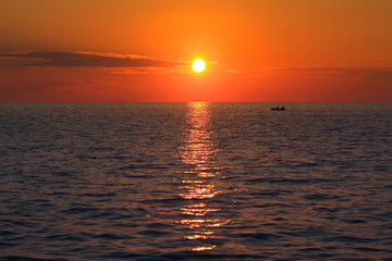 A boat sails along the coast of Cuba at a fiery sunset in the Caribbean Sea.