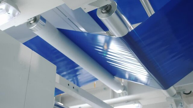 blue strip of adhesive tape transported by automatic production line conveyor with rollers in workshop close low angle shot