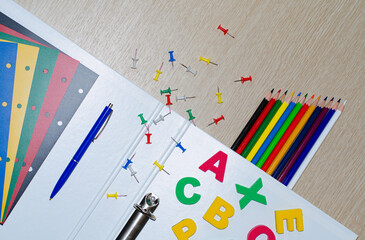 Colorful composition of vibrant color school supplies: colored pencils, papers, pens and english letters on the withe wooden background. Copy space. Flat lay. Back to school and education concept.