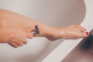 Close up of woman shaving legs in bathroom.