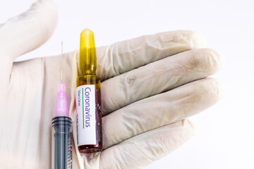 Coronavirus vaccine ampoule with an injection held in the palm covered by surgical glove.