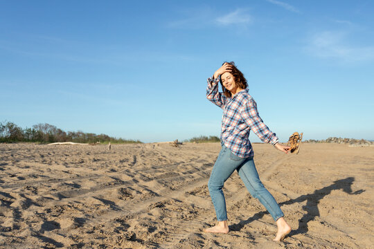 Outdoor atmospheric lifestyle photo of young beautiful  darkhaired woman in shirt  and jeans in on the beach, in the background the sea with sunset.