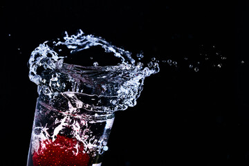 Strawberries fall into a glass of water. Water spills out of a glass. Carbonated drinks. Fruit drinks. Making a cocktail. Refreshing drinks. .Mix drinks. Water splashes. A stream of water.