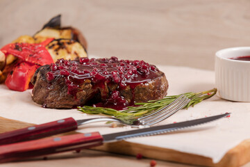 Steak with lingonberry sauce, full-bodied beef flavor, is on the wooden background.