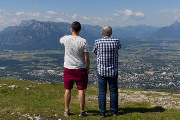 Obraz premium Father and Son standing on top of the mountain covered grass watching the city of Salzburg.