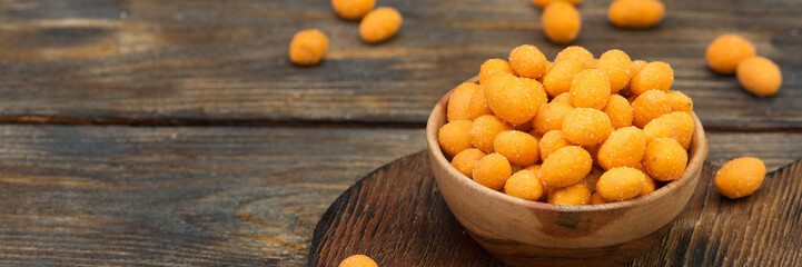 Fried peanuts in chili sauce in a wooden bowl on the brown kitchen table. Banner with space for text