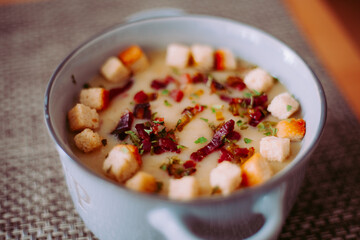 Zuppa soup di patate, con scalogno, erba cipollina, prezzemolo, pezzetti di prosciutto crudo e crostini di pane in una ciotola mono porzione in ceramica
