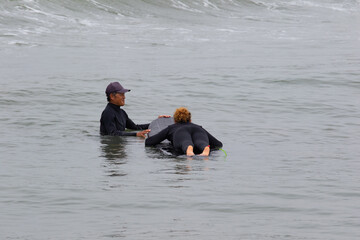 Young multiracial African American lady with amazing smile, freckles & frizzy hair & an Asian Japanese Surf Instructor having a surf lesson together in Chiba, Japan They are wearing black wetsuits.