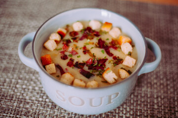 Zuppa soup di patate, con scalogno, erba cipollina, prezzemolo, pezzetti di prosciutto crudo e crostini di pane in una ciotola mono porzione in ceramica