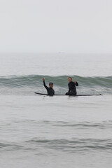 Young multiracial African American lady with amazing smile, freckles & frizzy hair & an Asian Japanese Surf Instructor having a surf lesson together in Chiba, Japan They are wearing black wetsuits.