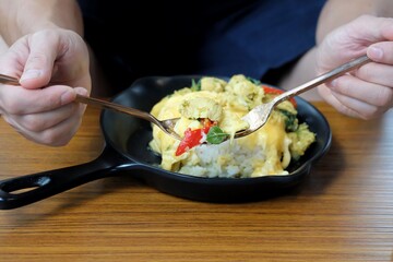  A male hand holding a spoon of green curry chicken with cooked rice and blurred a black plate on wooden dinning table 