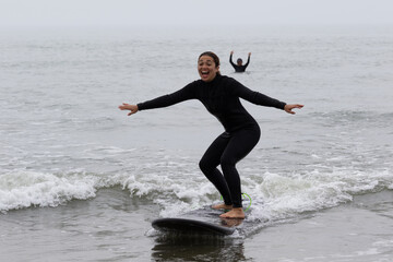 Young multiracial African American lady with amazing smile, freckles & frizzy hair & an Asian Japanese Surf Instructor having a surf lesson together in Chiba, Japan They are wearing black wetsuits.