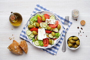 Greek salad with feta cheese, tomatoes, cucumbers, lettuce, olives and spices. Traditional greek cuisine. White rustic wooden table