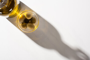top view of olive oil in bottle near green olives in bowl in shadow on white background