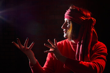 Portrait of middle age woman in red sweater and the turban of wizard or sorcerer on black...