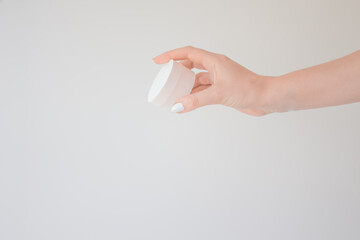 Round flacon for cream or lotion in female hand. Skincare and beauty concept. Mockup, copy space on a white background