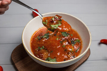 a plate of borsch with a spoon and a hand. chilli scattered around. gray wooden background