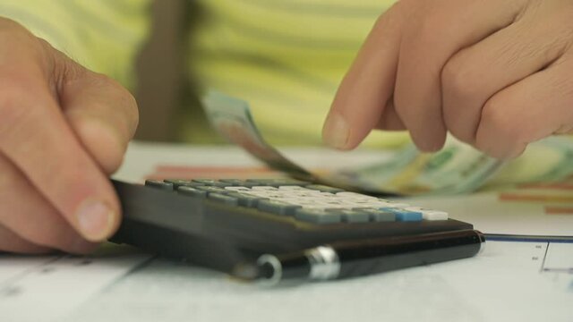pensioner hands count one hundred dollar banknotes on black outdated calculator at table with papers slow motion closeup
