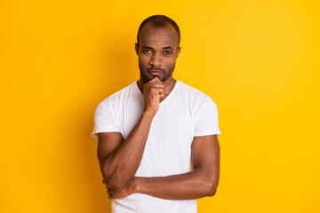 Photo of attractive dark skin guy hold arm on chin self-confident business man clever person wear casual white t-shirt blue jeans isolated bright vivid yellow color background