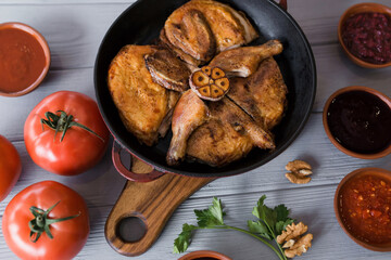 Grilled meat. Baked chicken in a pan close-up. Gray wooden background, spicy sauces and cutlery. Georgian cuisine