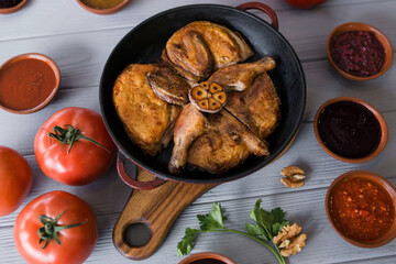 Grilled meat. Baked chicken in a pan close-up. Gray wooden background, spicy sauces and cutlery. Georgian cuisine