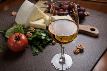 A glass of white wine close-up. Cheese and vegetables are sliced ​​on a board in the background. Georgian cuisine