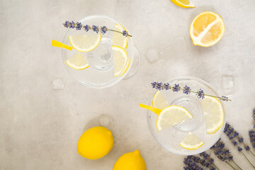Two glasses of citrus infused water with ice and lemon slices stand on a gray concrete background....