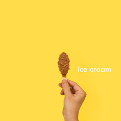 Mano sosteniendo un helado pequeño de chocolate con almendras de palo batuta sobre un fondo...