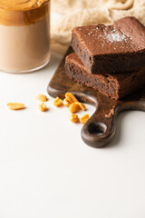 selective focus of delicious brownie pieces on wooden cutting board with peanuts near coffee in glass on white background