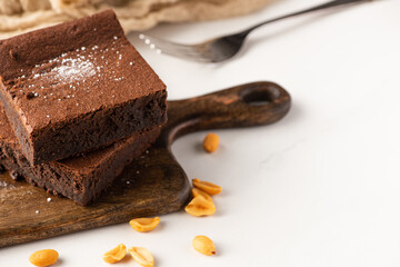 selective focus of delicious brownie pieces on wooden cutting board with peanuts on white background