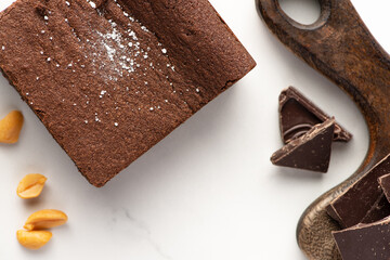 top view of delicious brownie piece near wooden cutting board, nuts and chocolate on white background