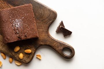 top view of delicious brownie piece on wooden cutting board with nuts and chocolate on white background