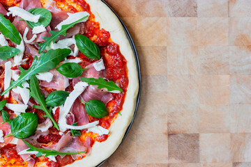 Top view of pizza Italian dish mediterranean food with ham, basil and Rocket green leaves, mozzarella on top with wooden background with copy space.