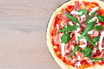 Top view of pizza Italian dish mediterranean food with ham, basil and Rocket green leaves, mozzarella on top with wooden background with copy space.