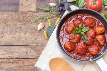Top view of homemade meatballs with tomatoes sauce and herbs with basil leaves, cheese and garlic laydown on wooden background with copy space for text.