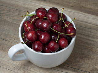 Fresh ripe cherries in a cup, on wooden background.