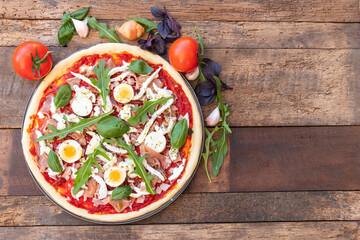 Top view of pizza Italian dish mediterranean food with ham, basil and Rocket green leaves, mozzarella on top with wooden background with copy space.