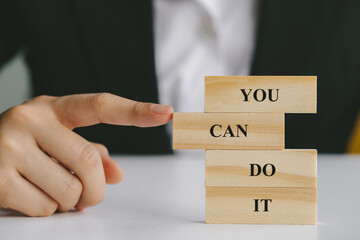 Hand of a businessman pushing wooden block into stack of blocks in a conceptual image. text you can do it.concept business succeed.