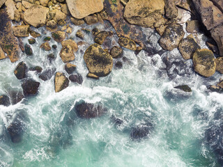 Aerial plane of a turquoise sea breaking over the rocks of the coast