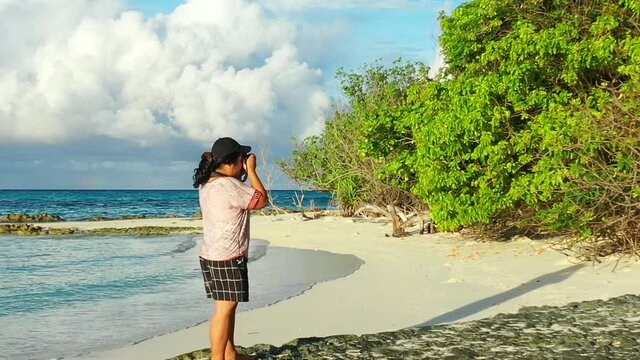 A woman taking photo of the trees by the sea shore, slowly panning to the left.